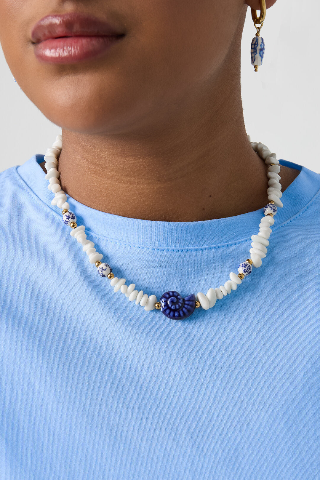 Collier composé de perles de pierre, de perles blanches ornées de fleurs bleues et d'un coquillage décoratif.