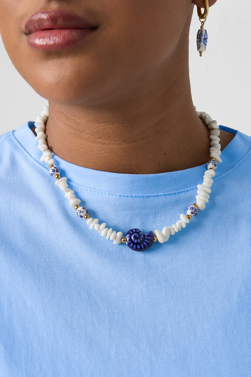 Collier composé de perles de pierre, de perles blanches ornées de fleurs bleues et d'un coquillage décoratif.
